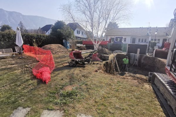 Travaux de terrassement en cours dans un jardin résidentiel en Suisse, avec pelleteuse, ouvrier et équipement de chantier pour future construction ou aménagement paysager