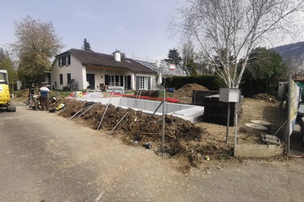 Travaux d’aménagement extérieur devant une maison en Suisse, avec installation d’une piscine enterrée, terrassement en cours et ouvriers sur le chantier