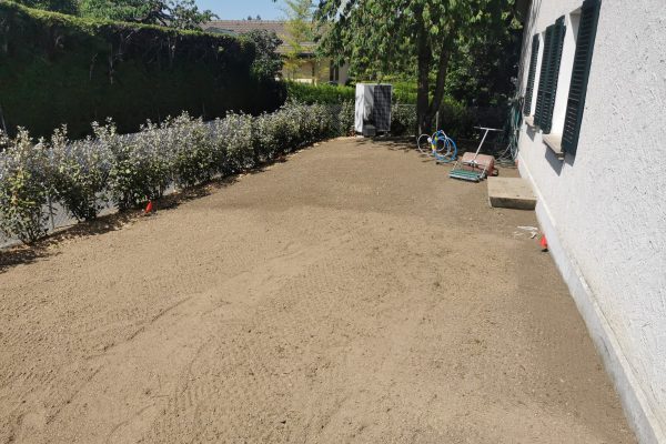 Terrain préparé devant une maison pour un aménagement extérieur, avec sol nivelé, haie et équipement de jardinage, en Suisse